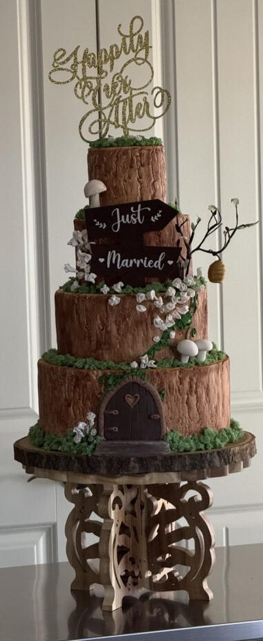 Rustic Woodland Wedding Cake Rustic tiered wedding cake with handcrafted fondant wood-grain details, flowers, greenery, and woodland accents.